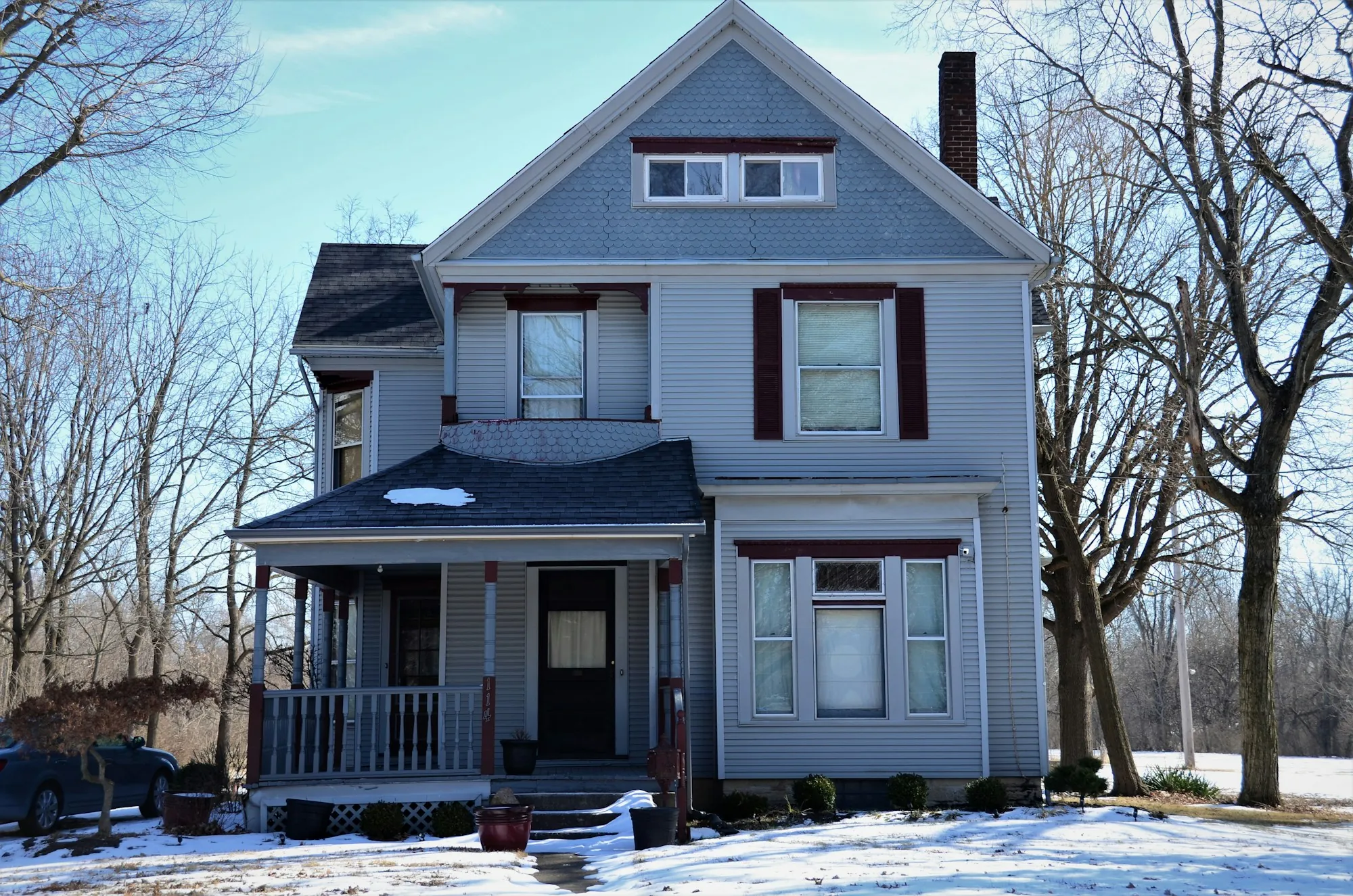 Gray two-story house with a shingle roof and front porch in winter